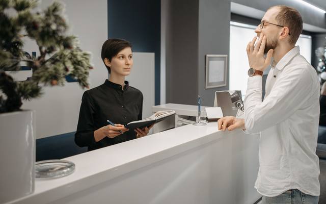 A receptionist helping a visitor at a clinic front desk