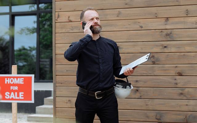 A real-estate agent on a phone call outside a house for sale